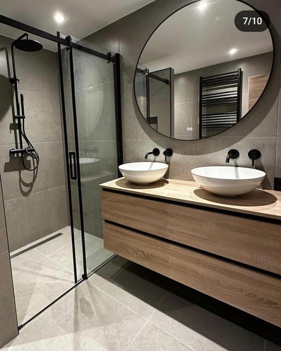 a bathroom with two sinks and a large round mirror above the sink, along with a walk in shower