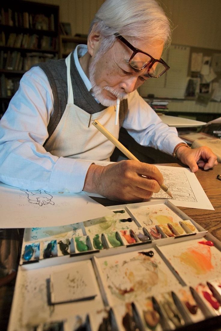 an older man sitting at a table working on some art