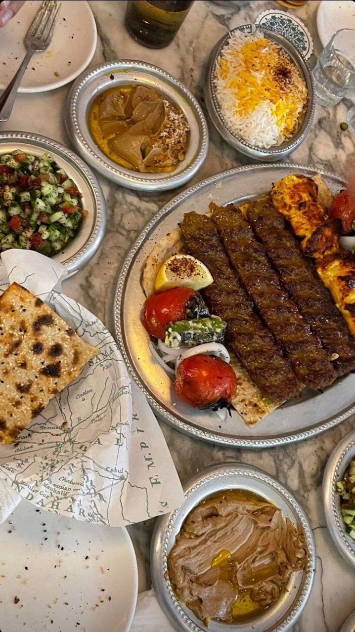 a table full of food including meat, salads and pita bread on plates