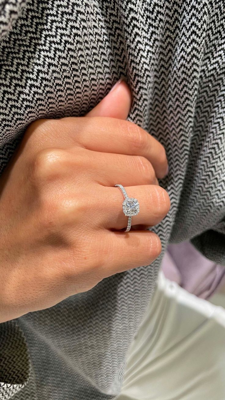 a woman's hand with a diamond ring on her left wrist, wearing a gray sweater and white pants