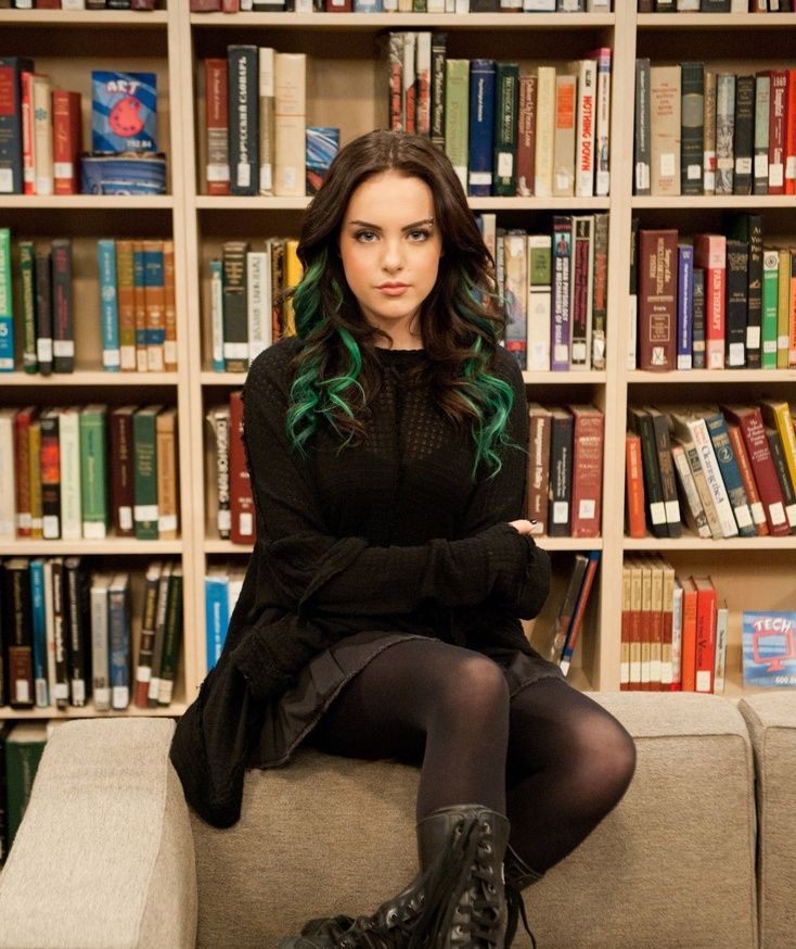 a woman with green hair sitting on a couch in front of bookshelves