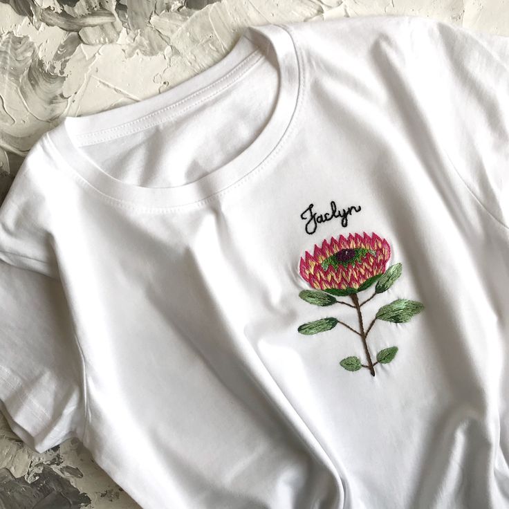 Botanical embroidery unusual women's t-shirt. This white t shirt has been embroidered by hand with a Protea flower on the pocket place. Name can be easily customized! The cute protea embroidery adds some flair and a handcrafted touch to a plain tee. The quality of the embroidery and t-shirt is superior, I guarantee! ;) If for some reason you will not be happy with you t-shirt (but you definitely will!) I will make full refund as I love my customers! DETAILS: All embroidery is done by hand in 100 White Cotton T-shirt As Gift, White Short Sleeve T-shirt With Floral Embroidery, White Floral Embroidery Short Sleeve T-shirt, White Floral Embroidered T-shirt, White Embroidered T-shirt For Summer, White Floral Embroidered Short Sleeve T-shirt, White T-shirt For Summer Gift, White Crew Neck T-shirt With Floral Embroidery, Trendy Cotton T-shirt With Custom Embroidery