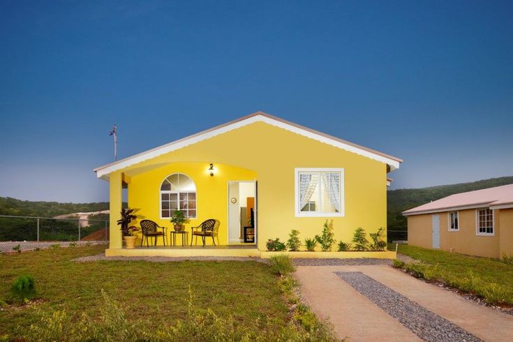 a small yellow house sitting on top of a lush green field