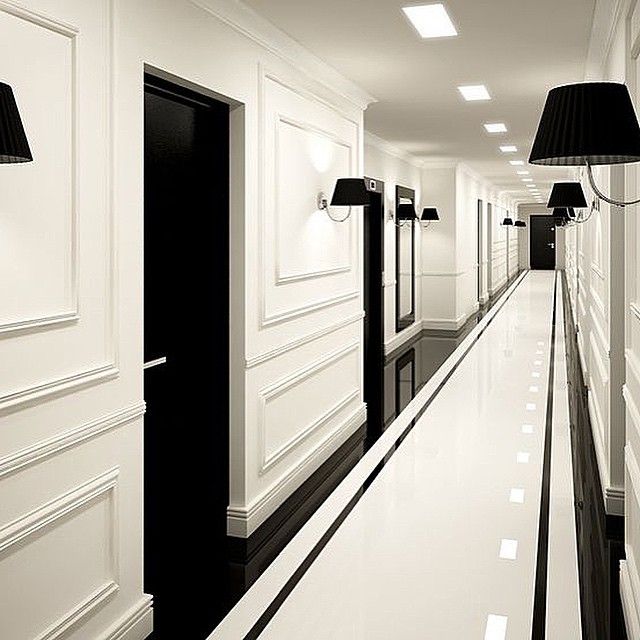 a long hallway with white walls and black lamps on either side of the corridor,