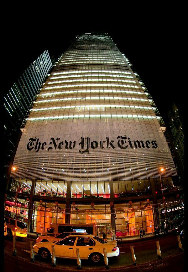 the new york times building lit up at night with cars parked in front of it