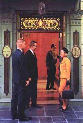 three men and two women are standing in front of a red door, talking to each other