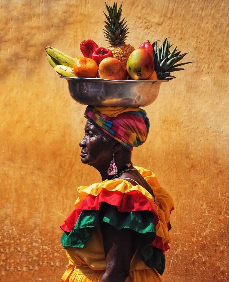 a woman carrying a bowl on her head filled with fruit