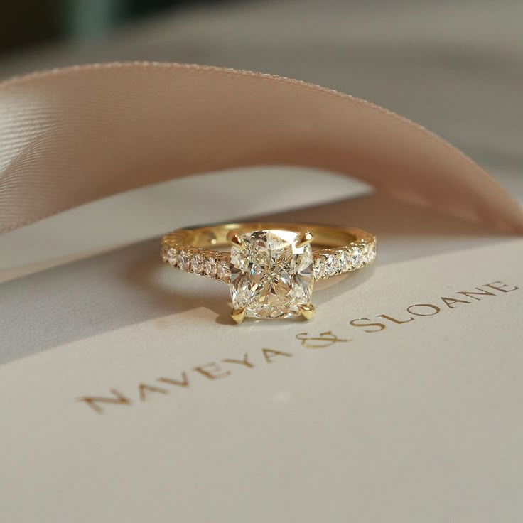 a diamond ring sitting on top of an open book with a ribbon around it's edge