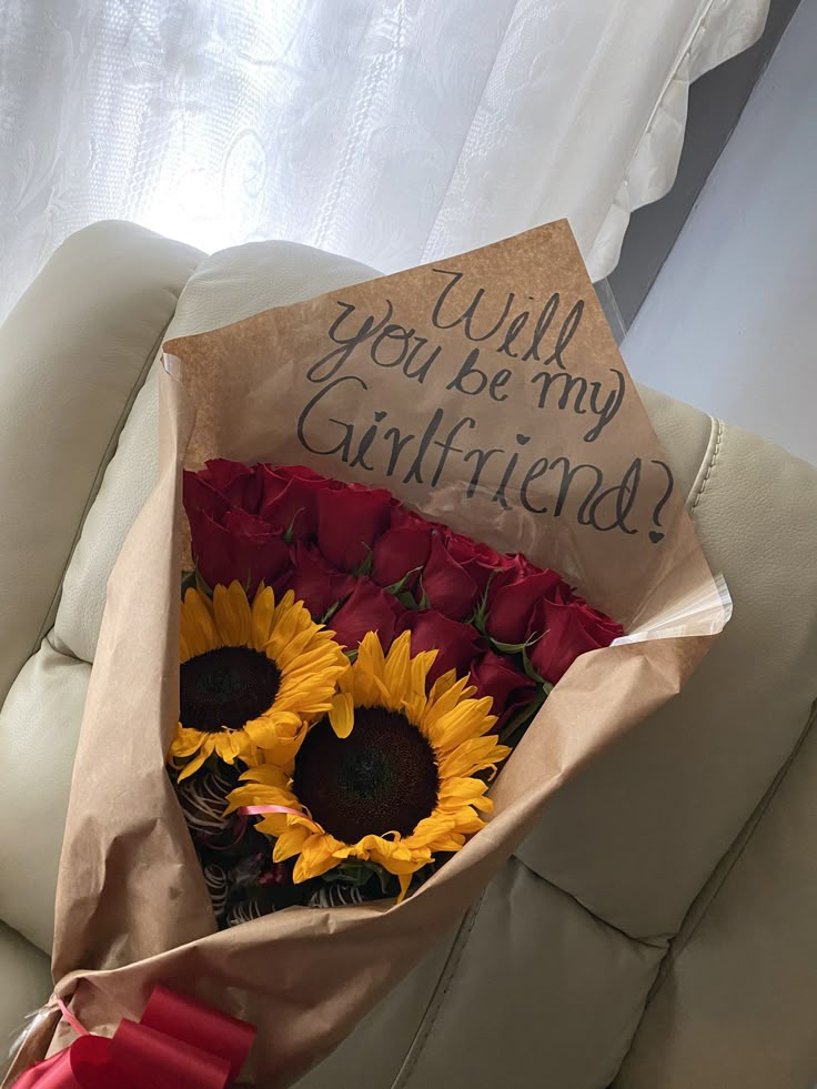 a bouquet of sunflowers and roses is wrapped in brown paper that says, will you be my girlfriend?