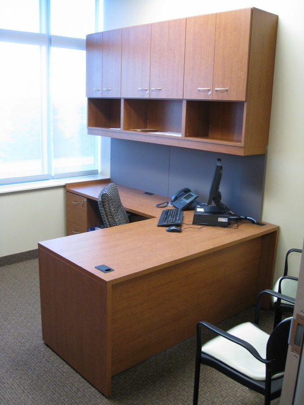 an empty office cubicle with a phone on the desk and chair in front of it