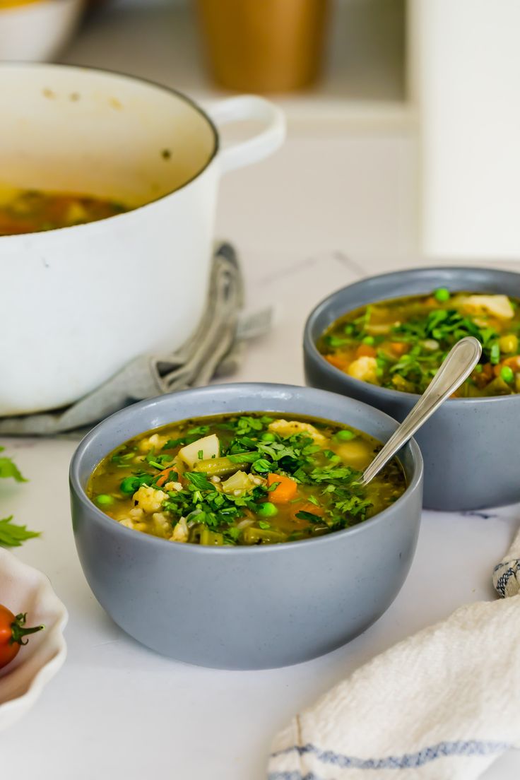 two bowls filled with soup sitting on top of a table next to a bowl of vegetables