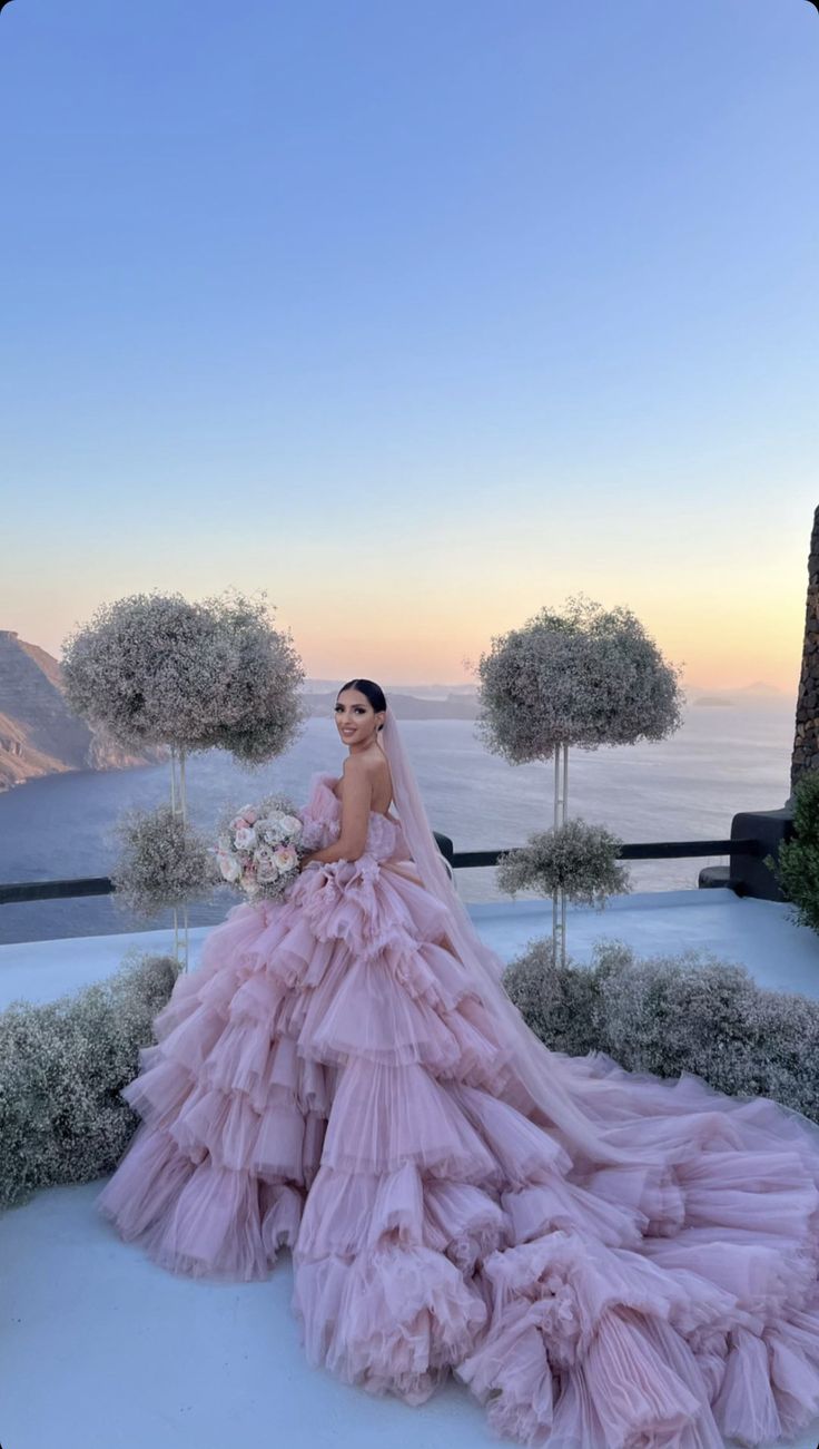 a woman in a pink wedding dress standing on top of a hill next to trees