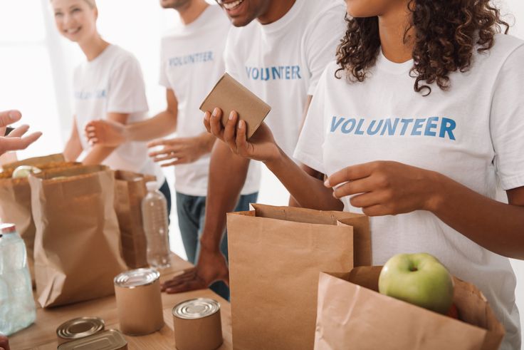 group of people standing around a table with bags and food