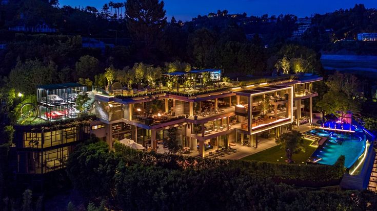 an aerial view of a mansion at night with lights on and pool in the foreground