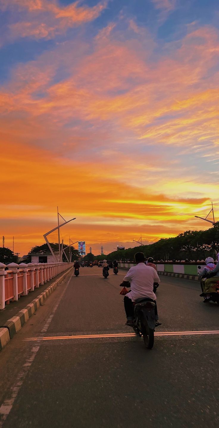 a person riding a motorcycle on the road at sunset with other motorcyclists