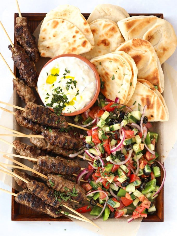 an assortment of skewered meats and vegetables on a plate with pita bread