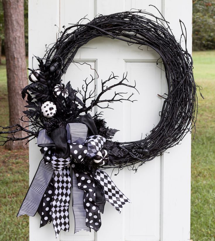 a wreath with black and white decorations is hanging on a door in front of some trees