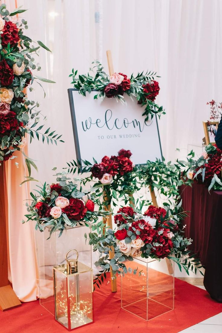 red flowers and greenery on display in front of a welcome sign at a wedding