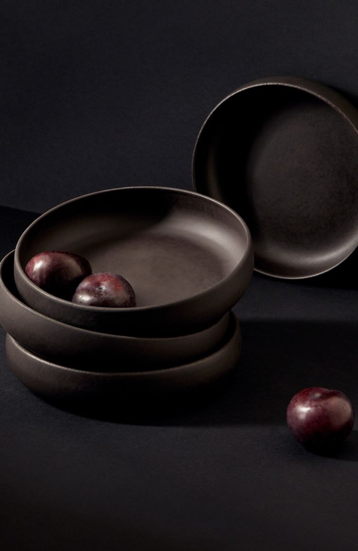 three bowls and two plates with fruit in them on a black surface, next to one another