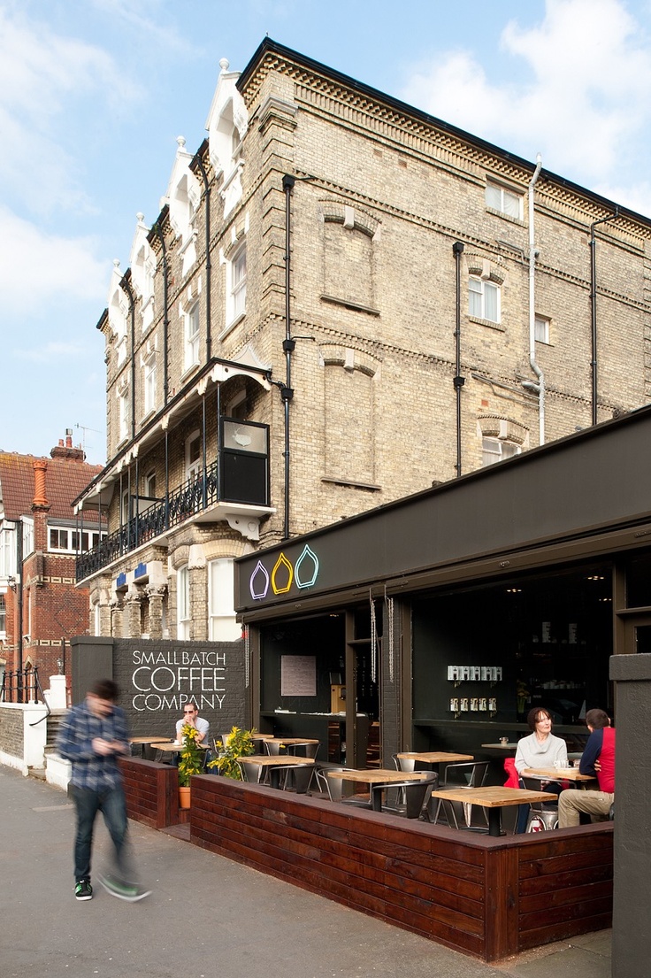 people are sitting at tables in front of a coffee shop on the side of the street