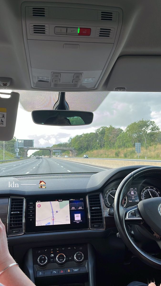 a woman driving a car on the road with her hand on the steering wheel, and another person using their cell phone