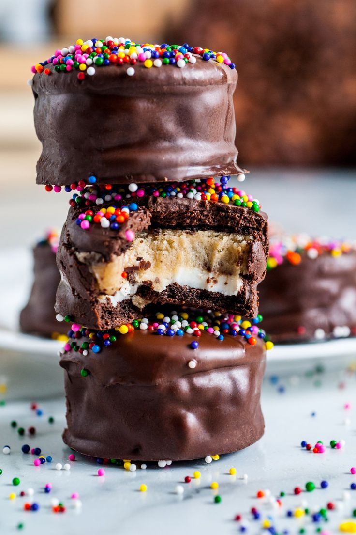 three chocolate covered desserts with sprinkles on them and one has a bite taken out of it