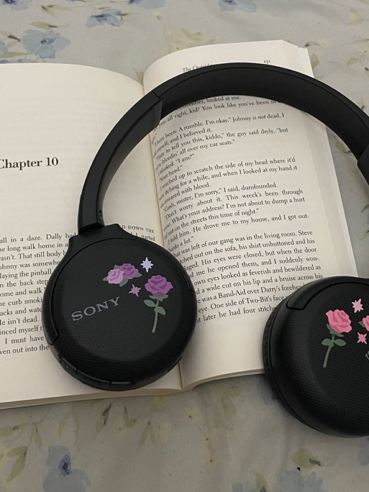 two black headphones sitting on top of an open book with pink flowers painted on them