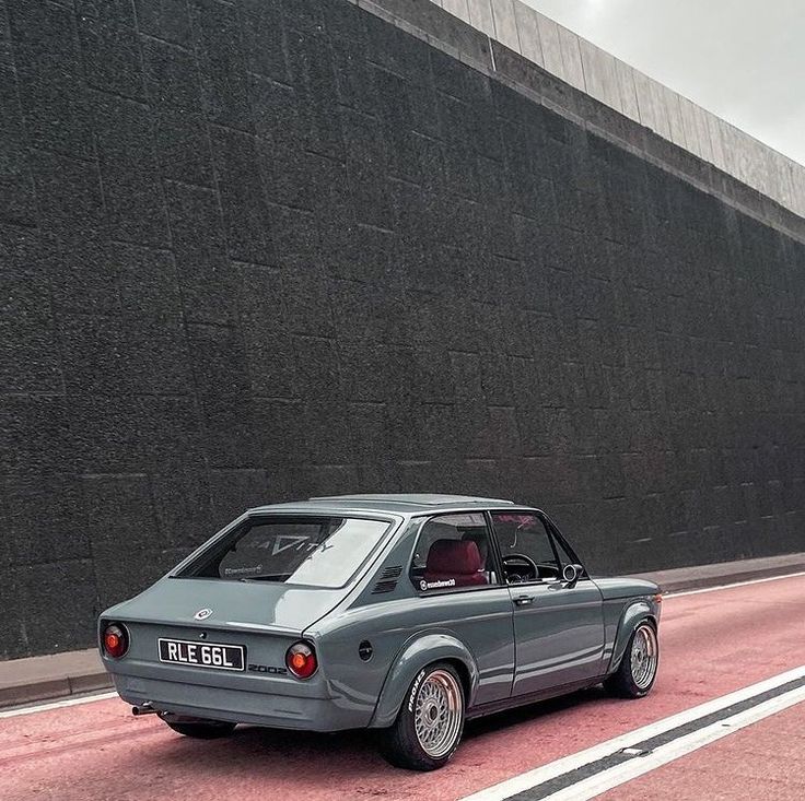 an old grey car is parked on the side of the road next to a wall