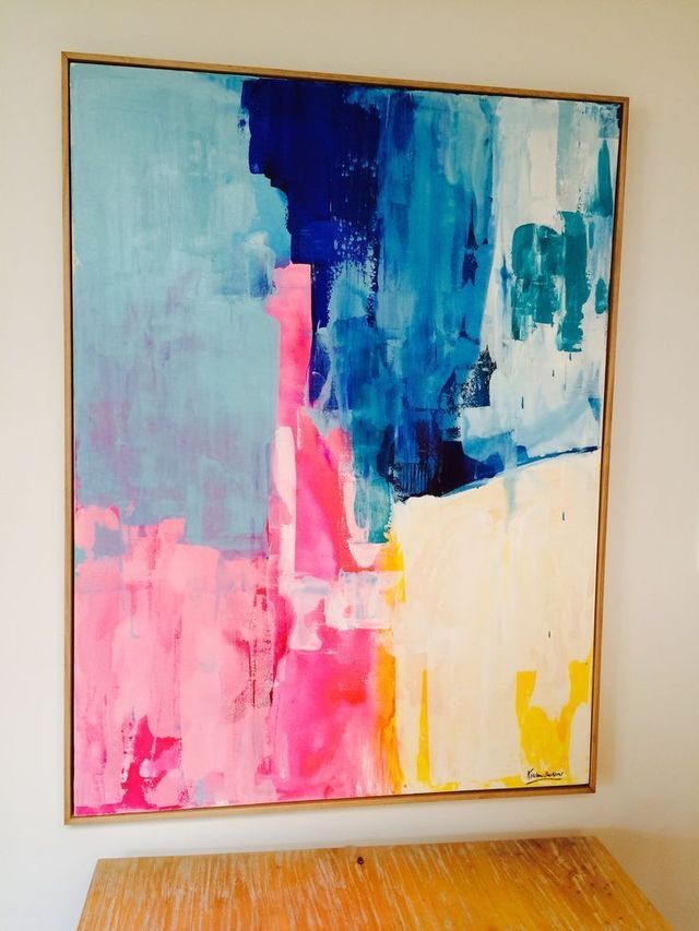 an abstract painting hangs on the wall above a wooden table in a room with white walls