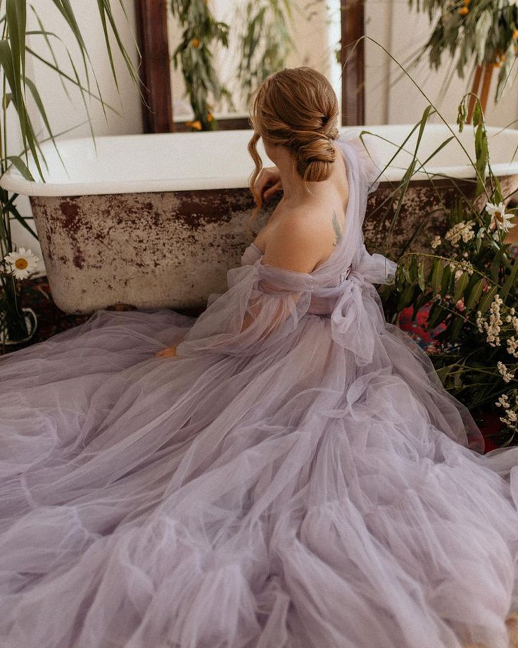 a woman in a purple dress sitting on the floor next to a tub with flowers