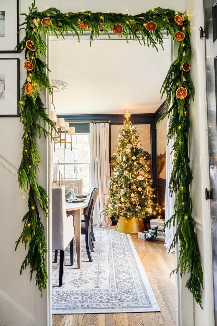 a christmas tree decorated with garland and lights is seen through an open door to the dining room