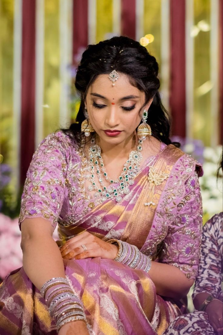 a woman in a purple and gold sari sitting down with her hands on her chest