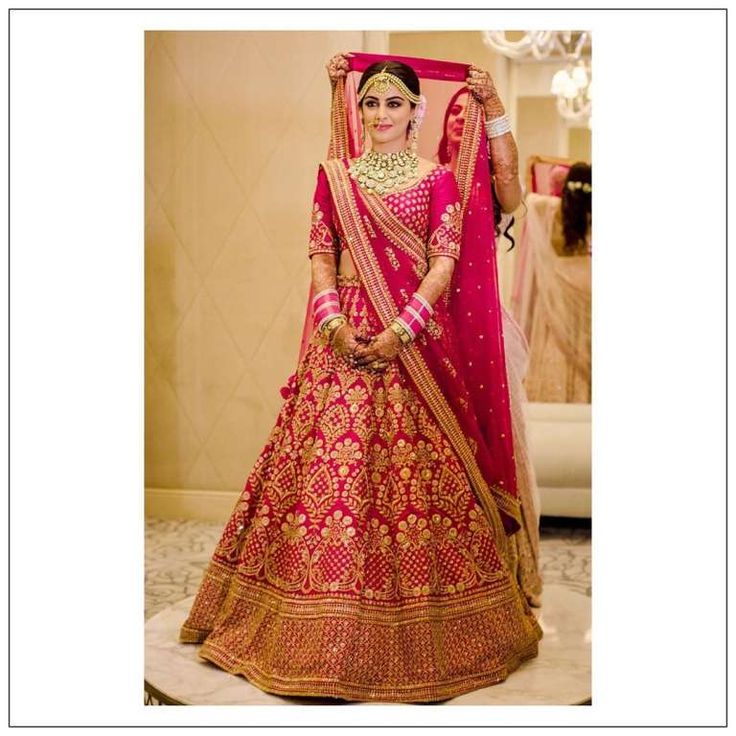 a woman in a red and gold bridal gown posing for the camera with her hand on her hip