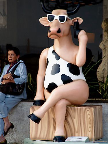 a statue of a cow sitting on top of a wooden block next to a woman