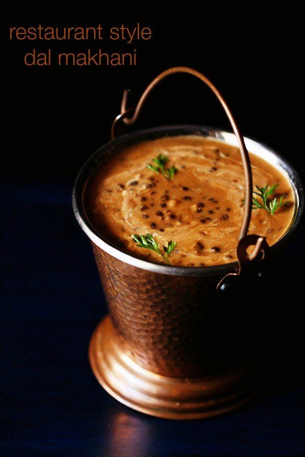 a small metal pot filled with food on top of a wooden table next to a black background