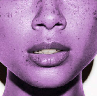 a woman with freckles on her face and purple makeup looks at the camera