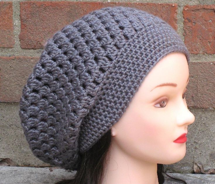 a mannequin head wearing a gray crocheted hat on top of a brick wall