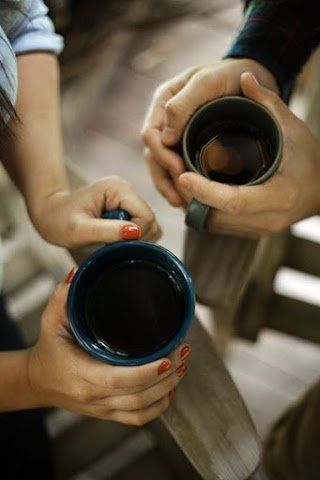 two hands holding a coffee cup on top of a wooden table next to another person