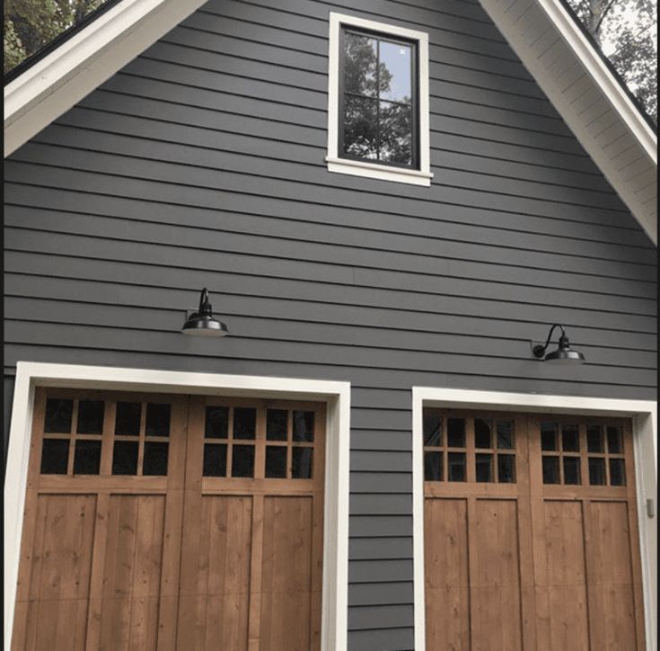 two brown garage doors are open in front of a gray house with white trim and windows