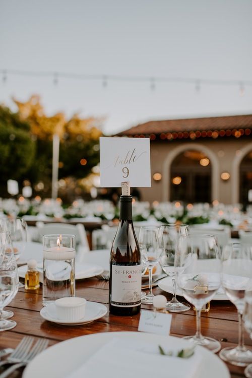 a bottle of wine sitting on top of a wooden table covered in glasses and plates