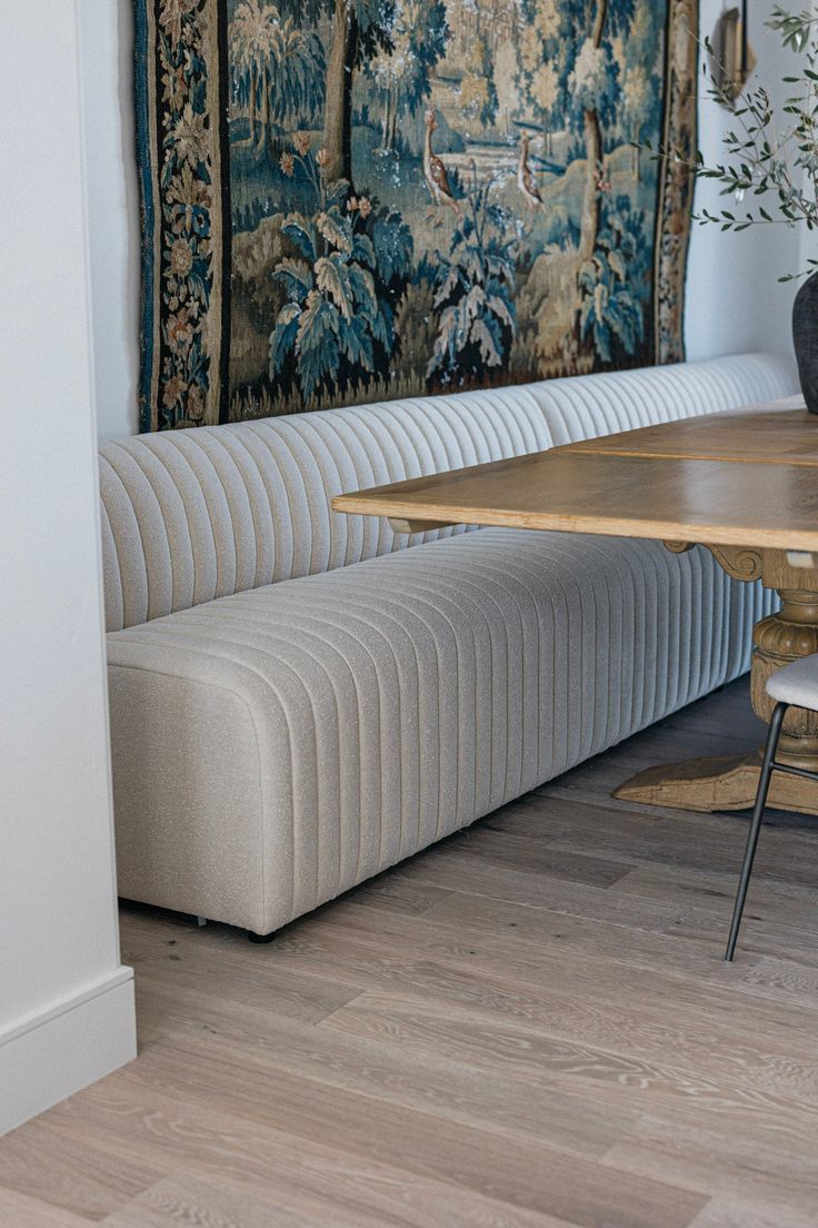 a room with a table, bench and tapestry on the wall above it in front of a couch