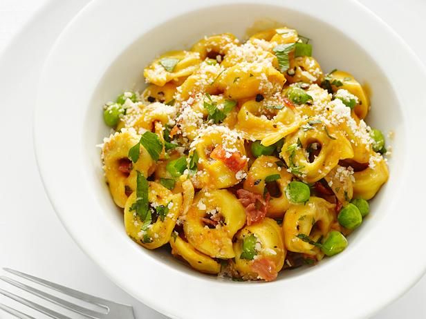 a white bowl filled with pasta and vegetables on top of a table next to a fork