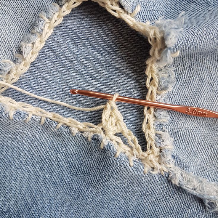 the crochet hook is next to an old pair of jeans that have been stitched together