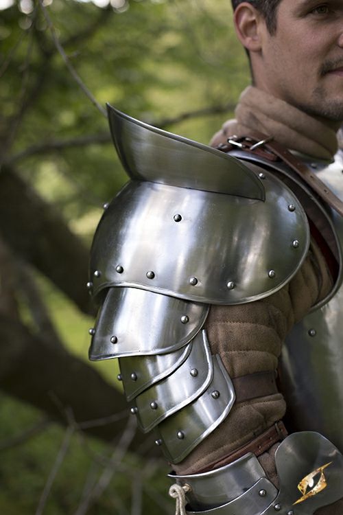 a man dressed in armor standing next to a tree with his hand on his hip