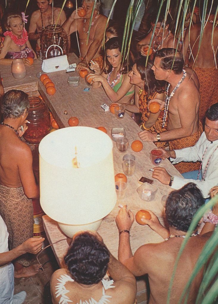 a group of people sitting around a table with oranges on it and candles in the middle