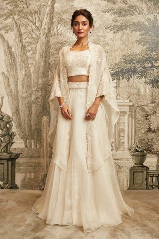 Ivory asymmetric cape featuring tonal resham embroidered floral jaali motifs, cut-out border, embellished by beads and sequins. Comes with padded inner blouse and embroidered waistband lehenga. - Aza Fashions Elegant Wedding Lehenga With Cape, Cape Style Lehenga For Wedding, Fitted Cape Set For Wedding, Elegant Lehenga With Sheer Dupatta And Cape, Festive White Lehenga With Cape Sleeves, Elegant White Lehenga With Cape Sleeves, Festive Embellished Lehenga With Cape Sleeves, Embellished Choli With Cape Sleeves, Unstitched Blouse Lehenga With Cape Sleeves