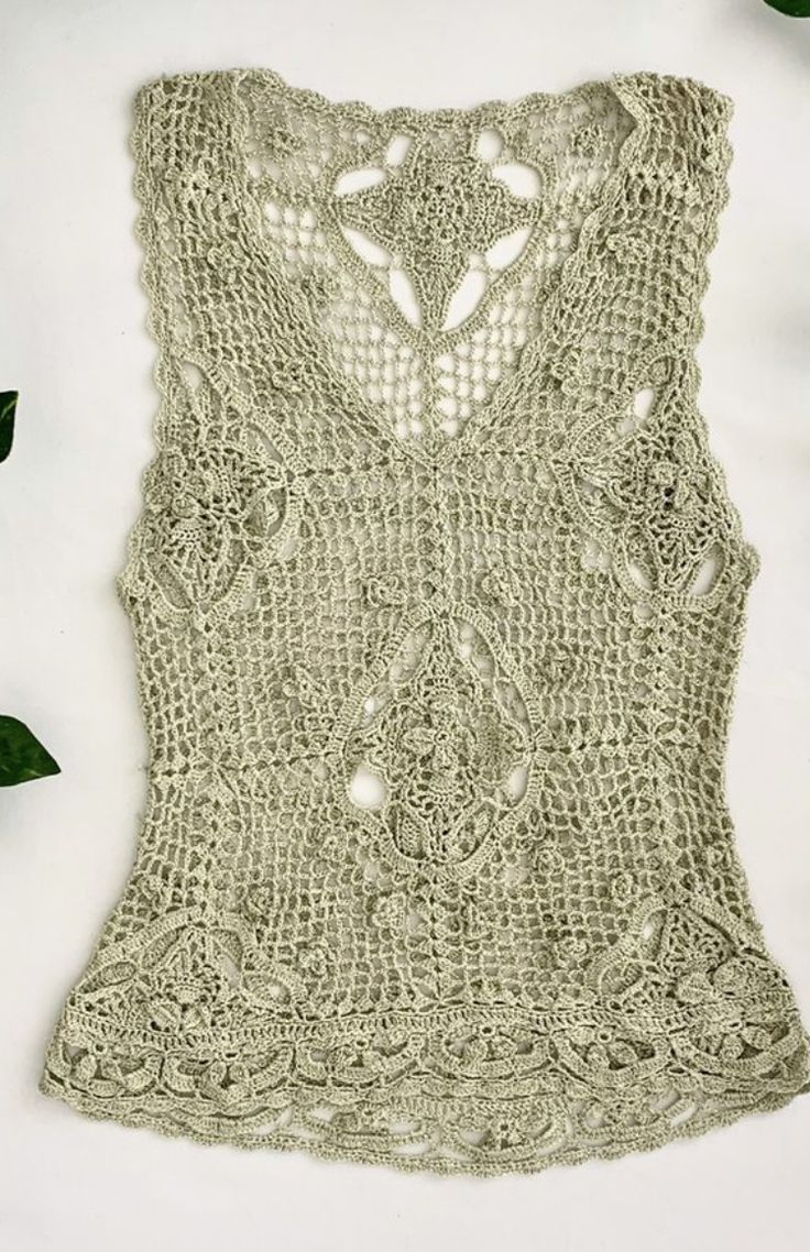 a crocheted top is shown with green leaves on the table next to it