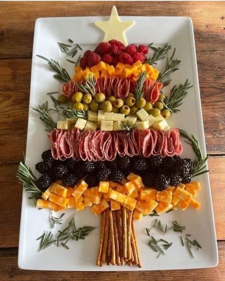 a christmas tree made out of different types of food on a white platter with olives, pineapples and other fruits