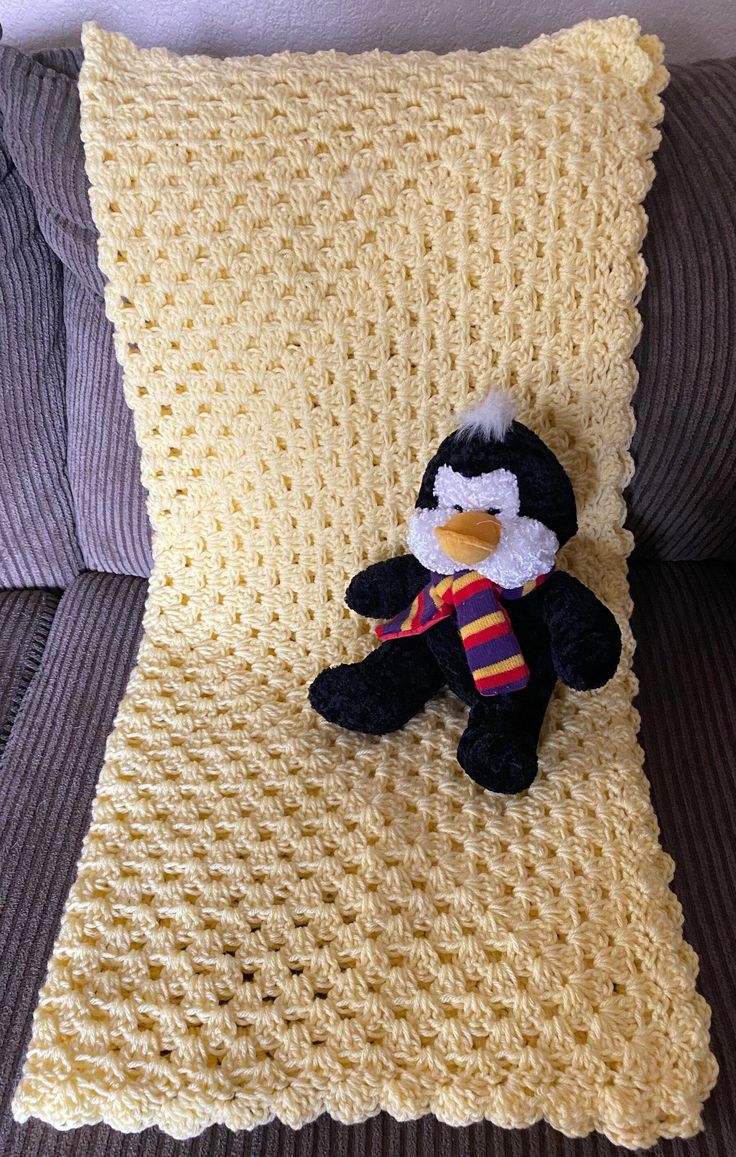 a crocheted pillow with a stuffed penguin on it, sitting on a couch