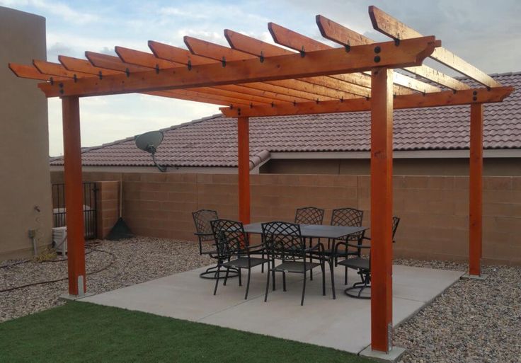 an outdoor dining area with table and chairs under a pergolated arbor in front of a house